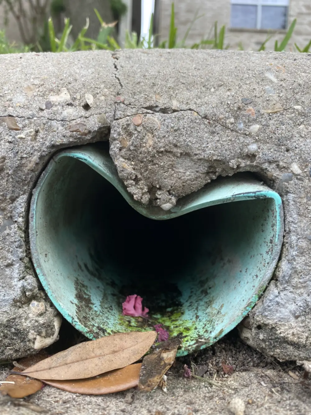 French drain outlet pipe crushed where it exits through a concrete curb