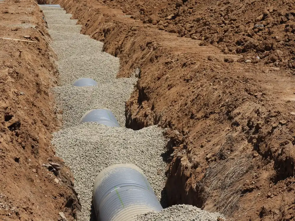 Corrugated drain pipe bedded in washed gravel inside a drainage trench in Collin County TX